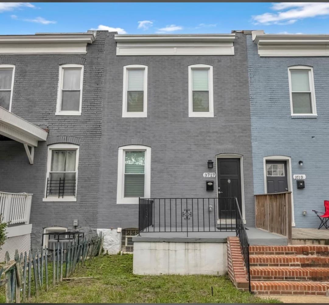 Grey brick row house with white-trimmed windows, black door, and a small front porch.