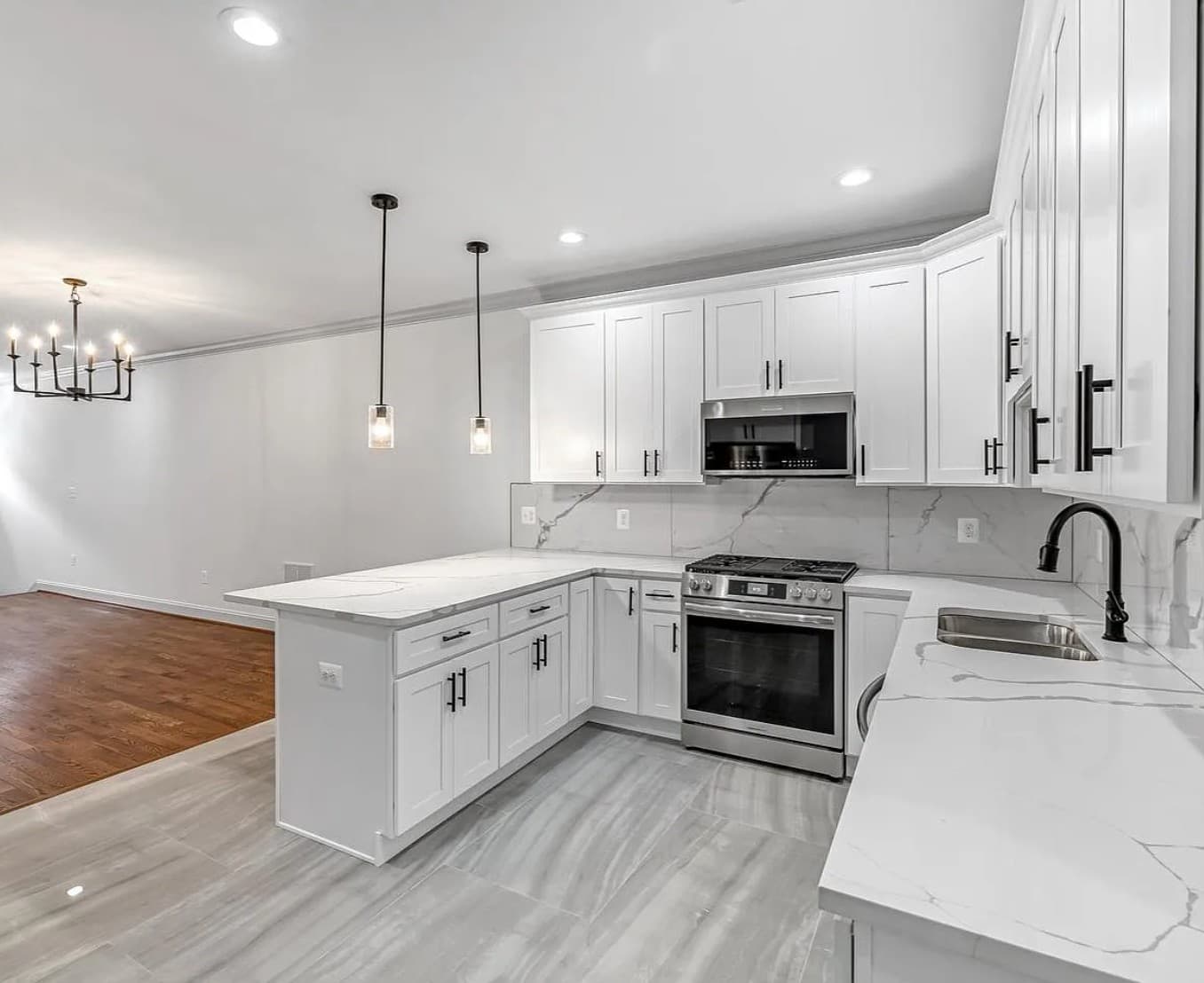 Modern white kitchen with marble countertops, stainless steel appliances, black hardware, and pendant lighting.