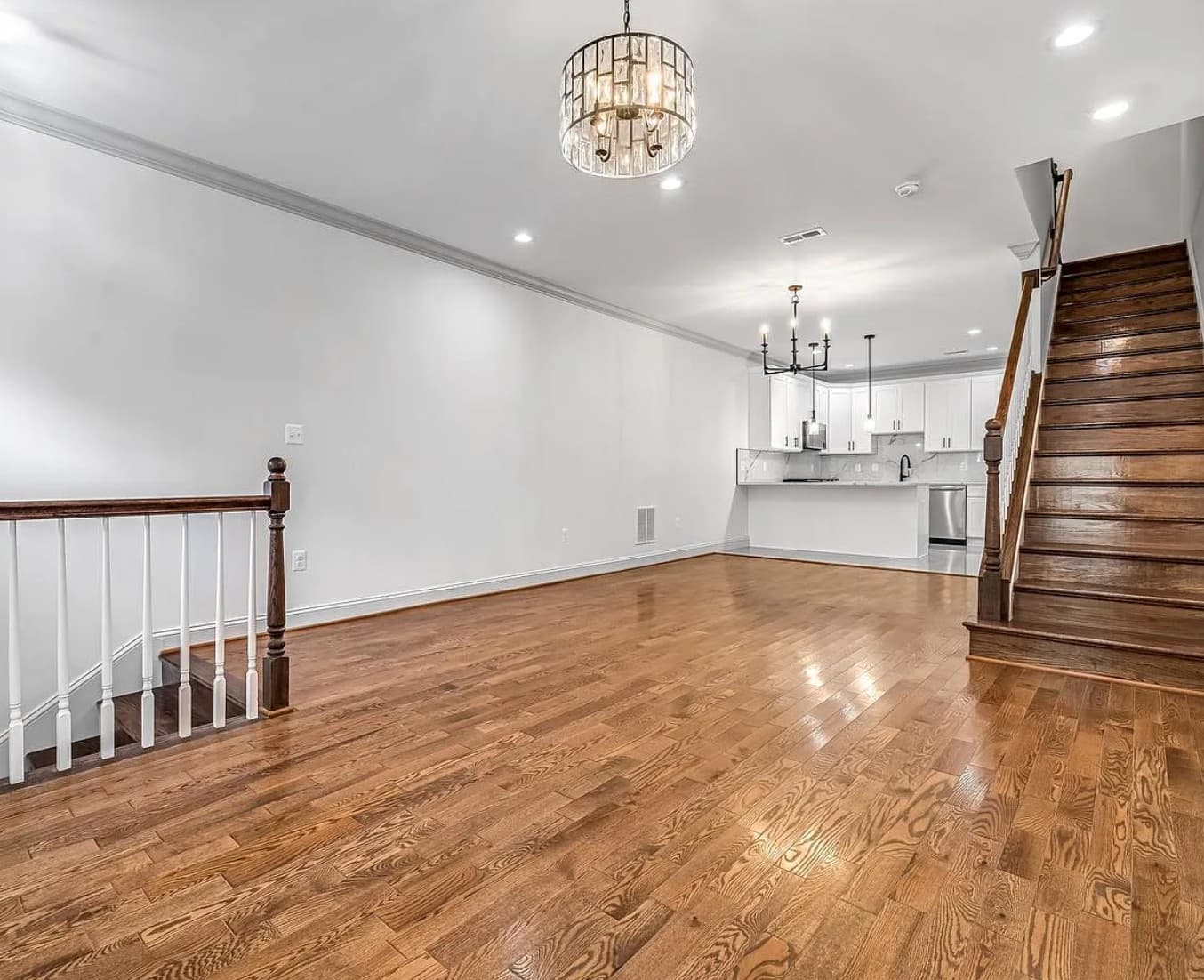 Spacious open-concept living area featuring hardwood floors, a white kitchen, and dual wooden staircases.
