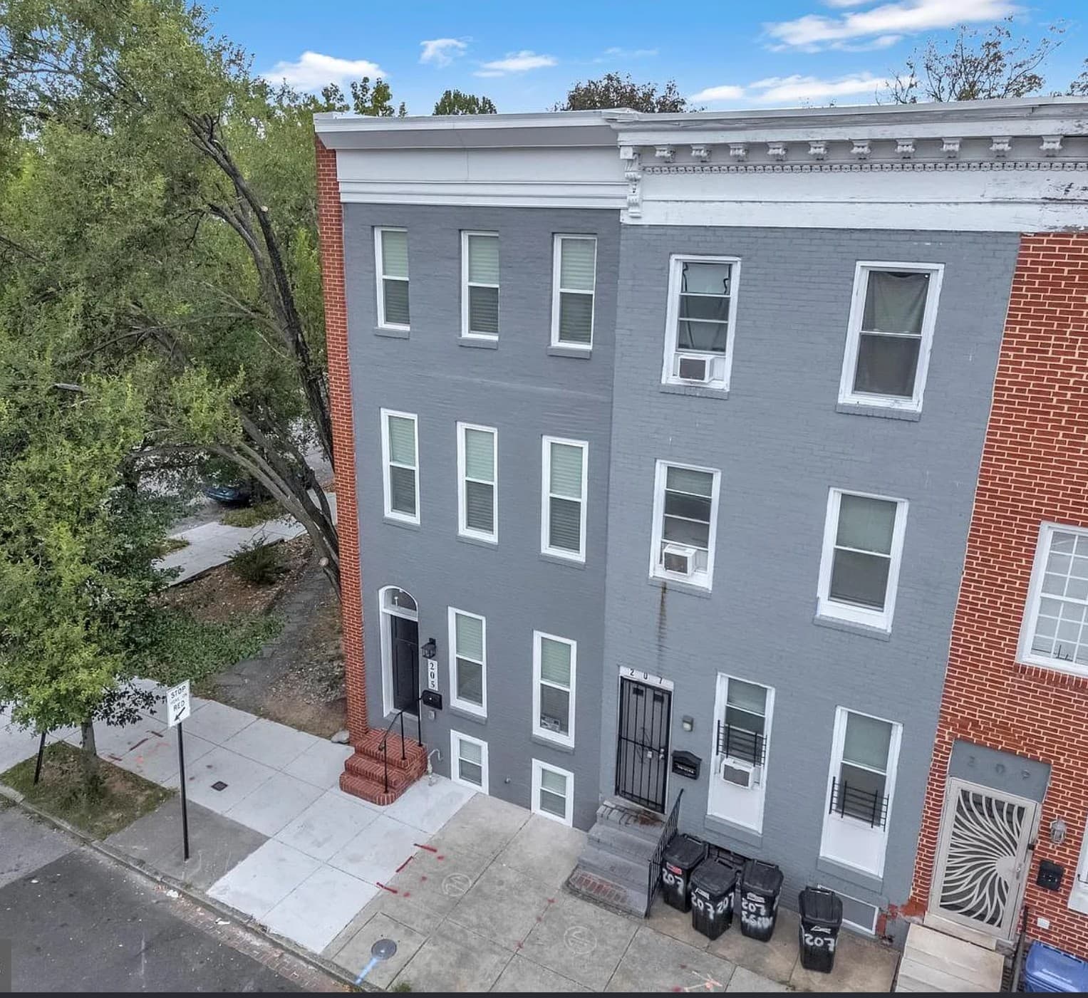 Three-story grey brick row house with white trim and windows on an urban street.