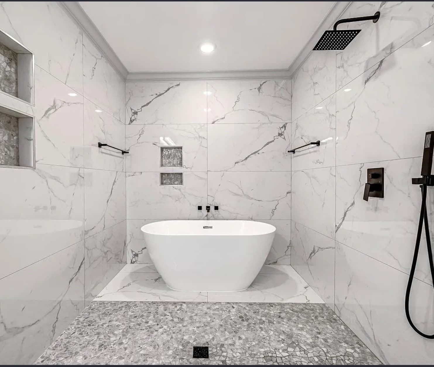 Modern bathroom featuring white marble walls, a freestanding tub, pebble floor, and black fixtures.